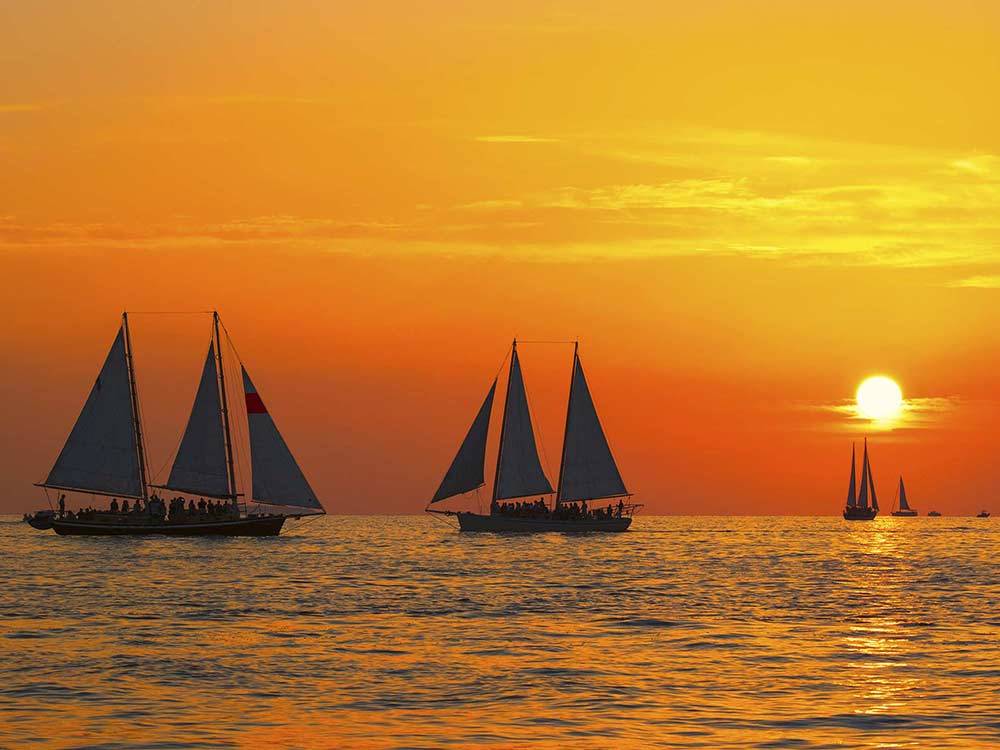 Sail boats cruising on the ocean with glowing orange sunset in background at BOYD'S KEY WEST CAMPGROUND