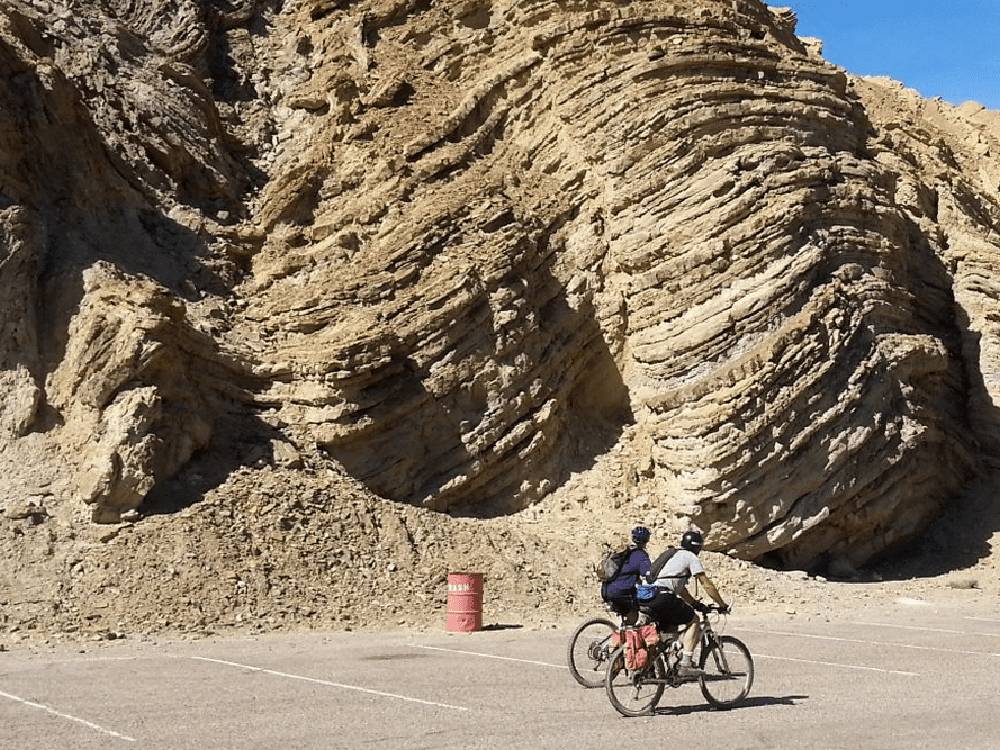 Two bicycle riders going past a large rock formation