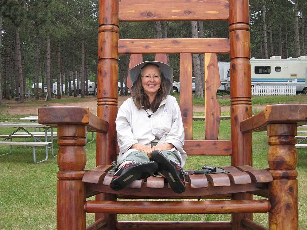 Lady sitting in big chair at campsite with trailers at LAKE DUBAY SHORES CAMPGROUND