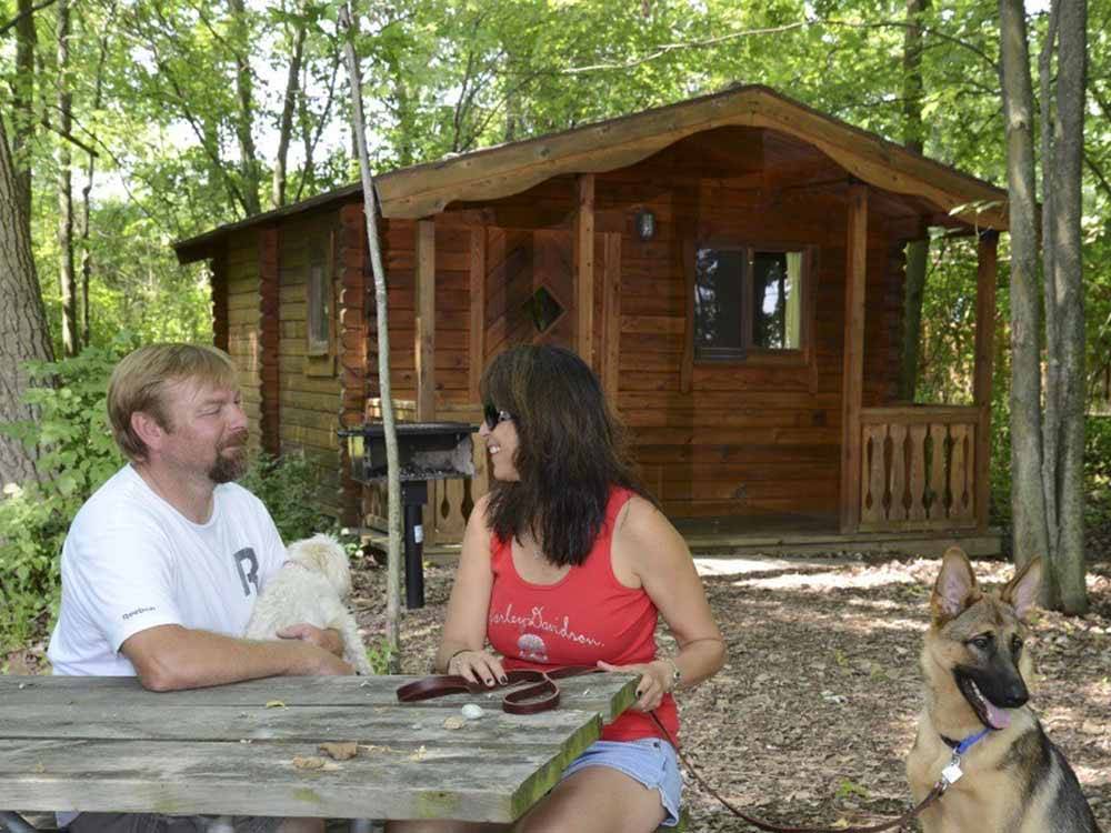 A couple sitting in front of a rustic rental cabin at INDIAN CREEK CAMP & CONFERENCE CENTER