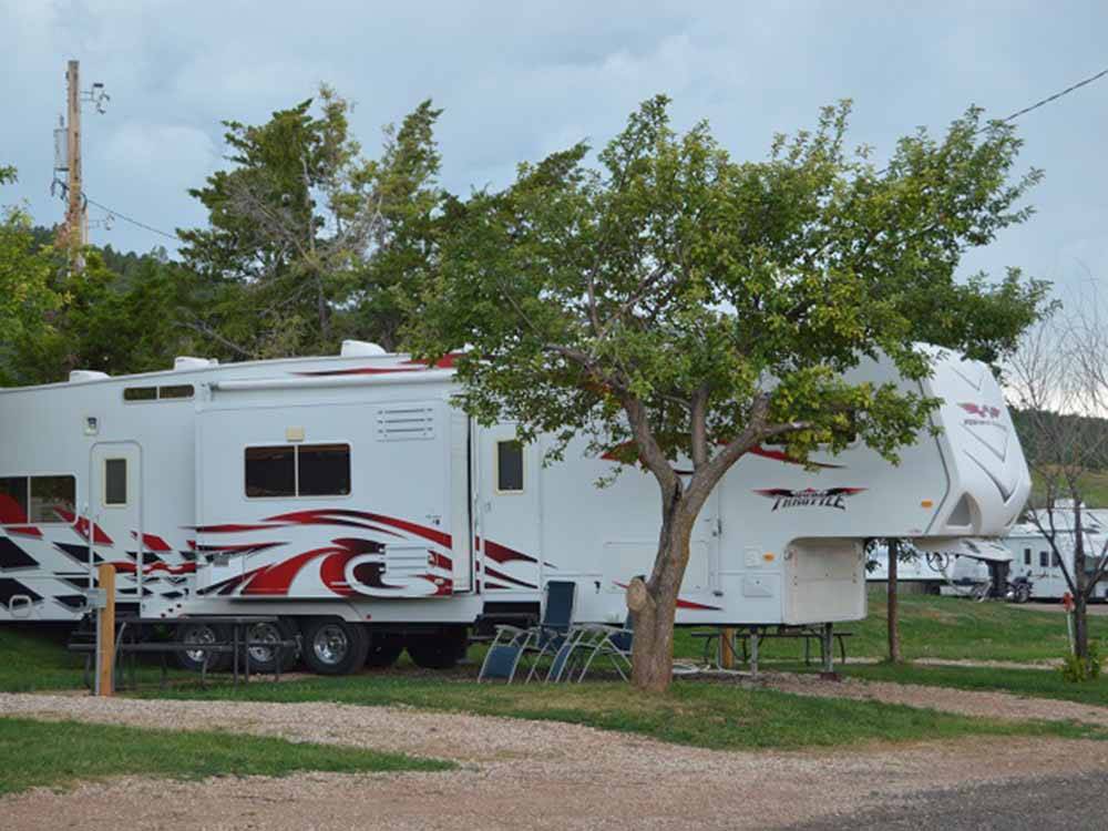 Triple-axle fifth-wheel with tree in foreground at NO NAME CITY LUXURY CABINS & RV PARK
