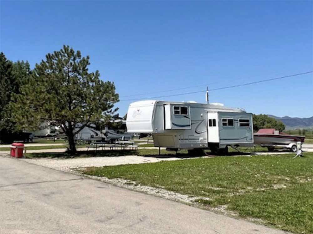 A fifth wheel trailer and boat parked in a gravel site at MOUNTAIN ACRES RV PARK