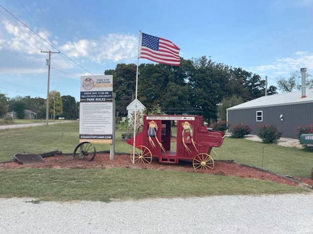 An old stagecoach with scarecrows in it next to a flag