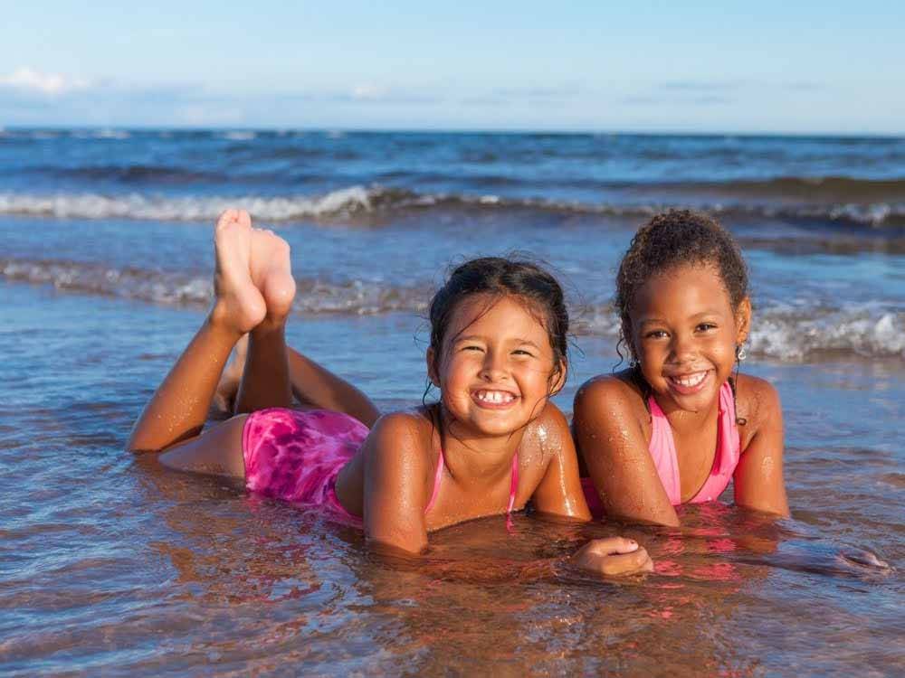 Two girls laying in the waves on the beach at PEI PROVINCIAL PARKS