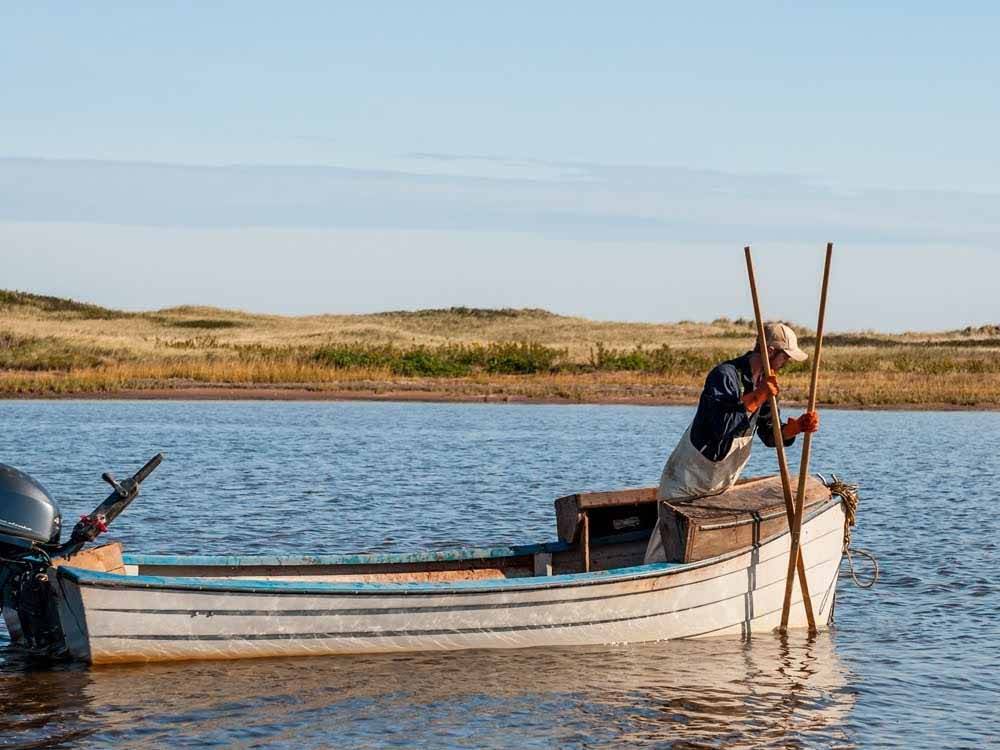 A man with two longs sticks in a boat at PEI PROVINCIAL PARKS
