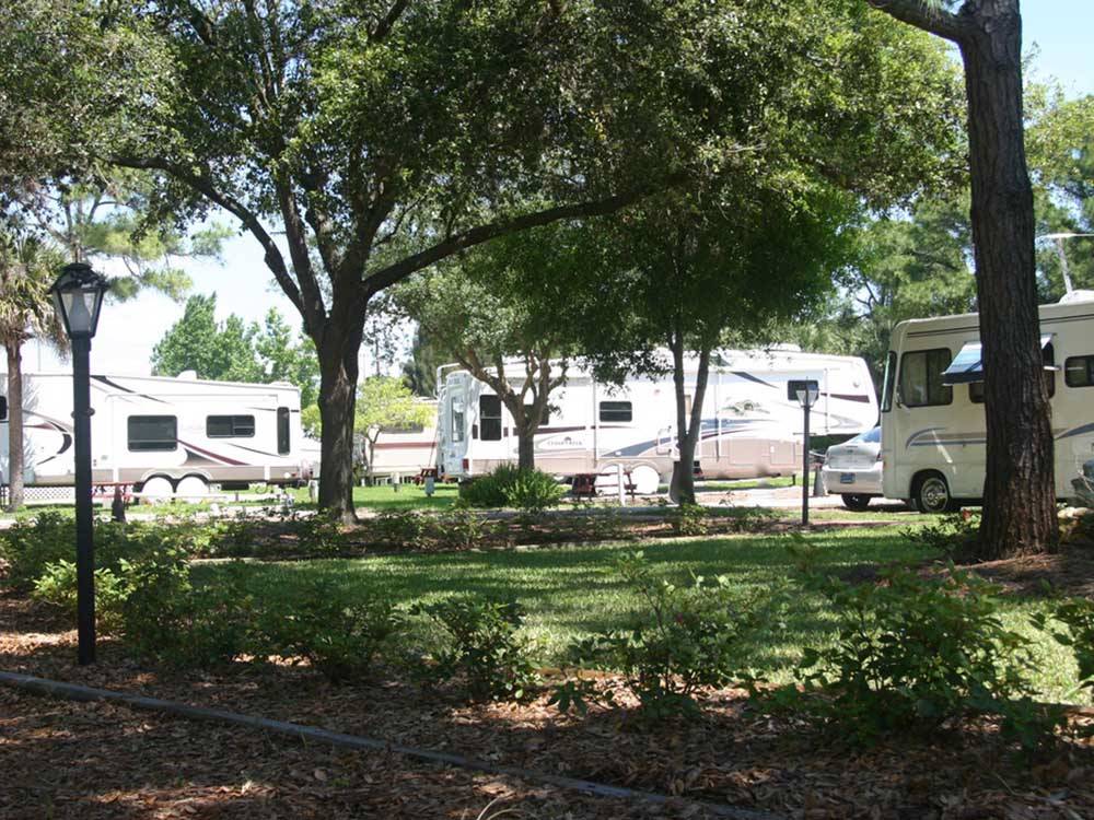 Motorhome and trailers parked by a shady area at WHISPERING PINES