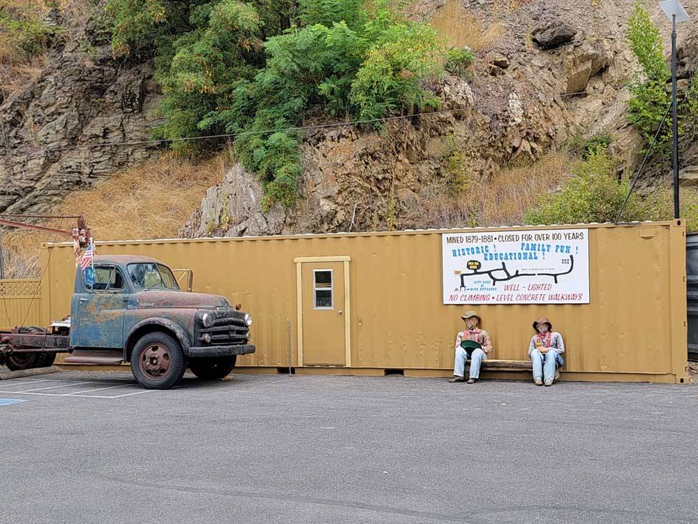 Two men statues sitting under a sign at CRYSTAL GOLD MINE & RV PARK