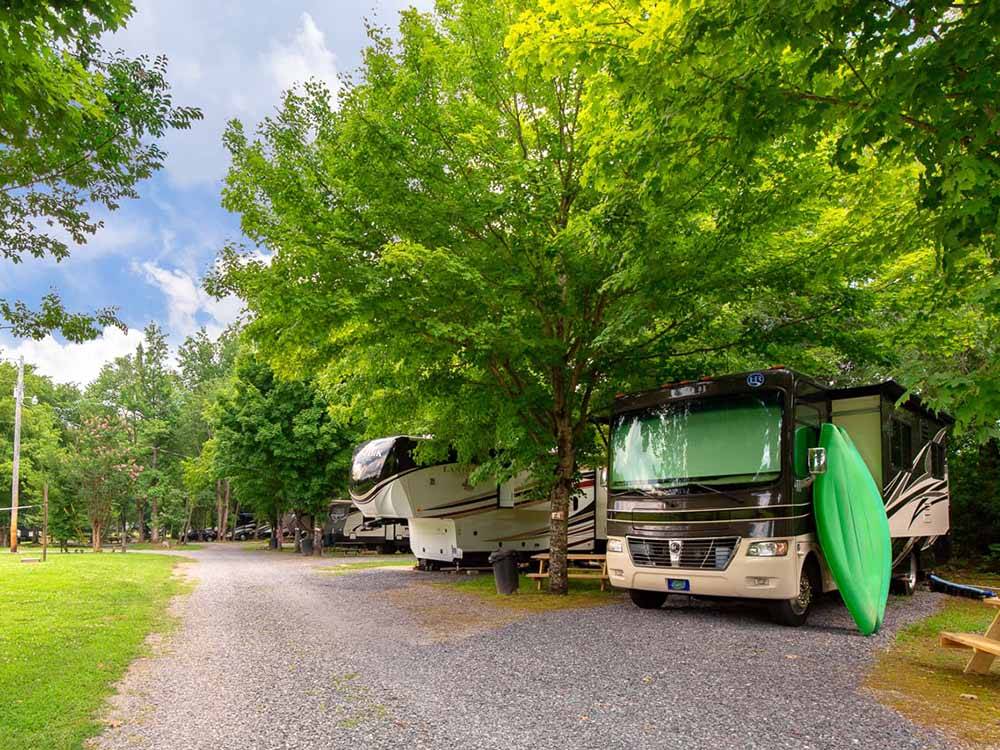 A green kayak leans against a Class A Motorhome parked in a well-shaded back-in RV space at TRIPLE CREEK CAMPGROUND
