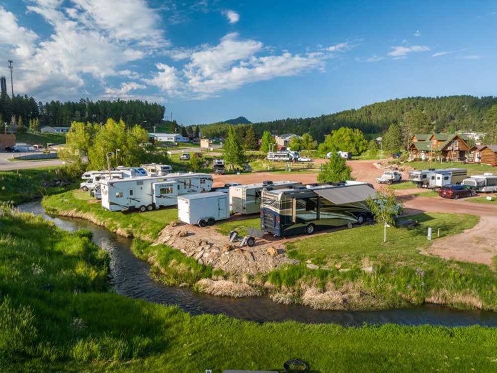 Motorhomes and trailers backed in by the water at BLACK HILLS TRAILSIDE PARK RESORT