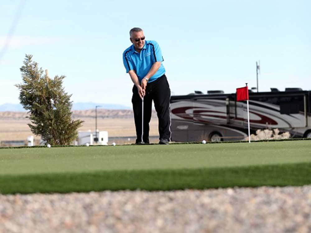 A man playing golf next to a motorhome at ROUTE 66 RV RESORT