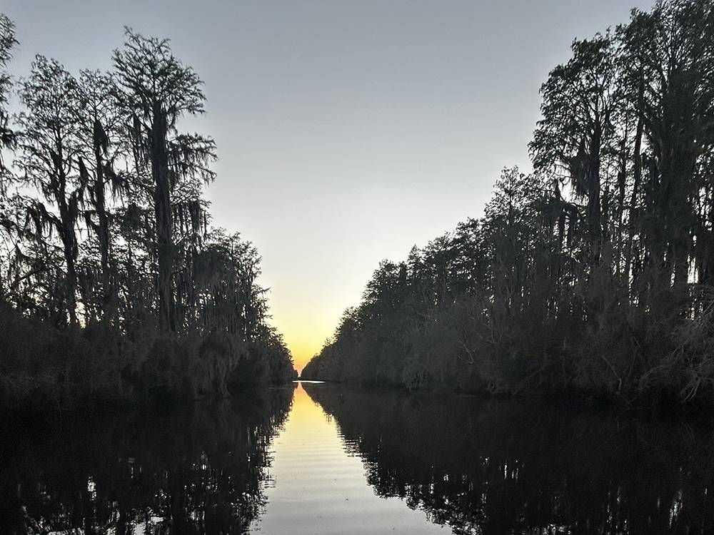 A calm river lined by trees at dusk