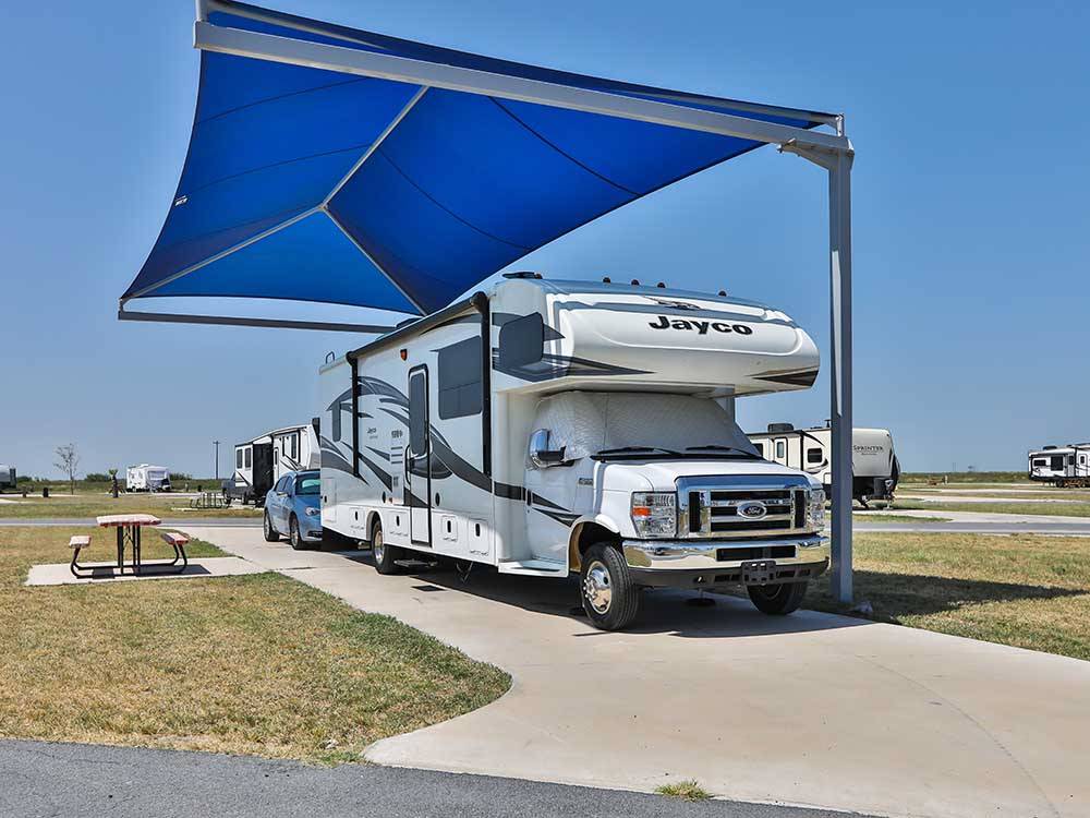 A Class C motorhome parked under a shade at JETSTREAM RV RESORT - TROPICAL TRAILS