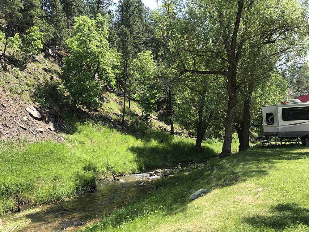 Trailer camping on grass next to stream at RUSHMORE VIEW RV PARK