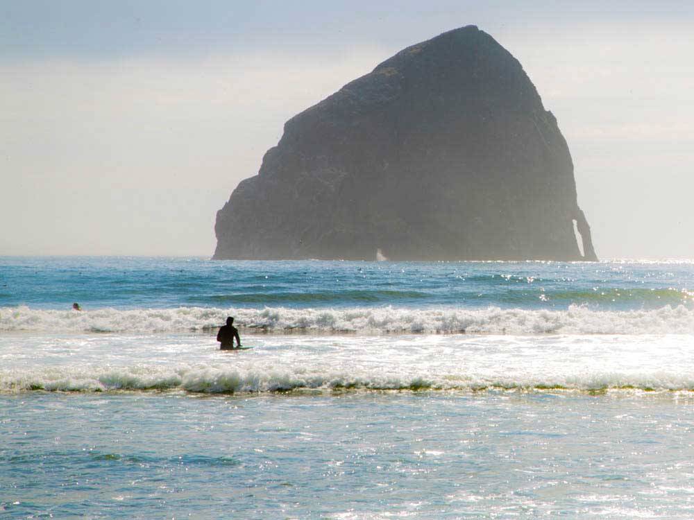 Man with paddle in ocean and big rock at THOUSAND TRAILS PACIFIC CITY