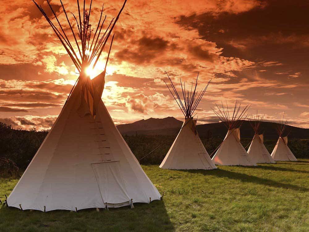 A row of teepees with a beautiful sunset in the background at CHEWING BLACK BONES CAMPGROUND
