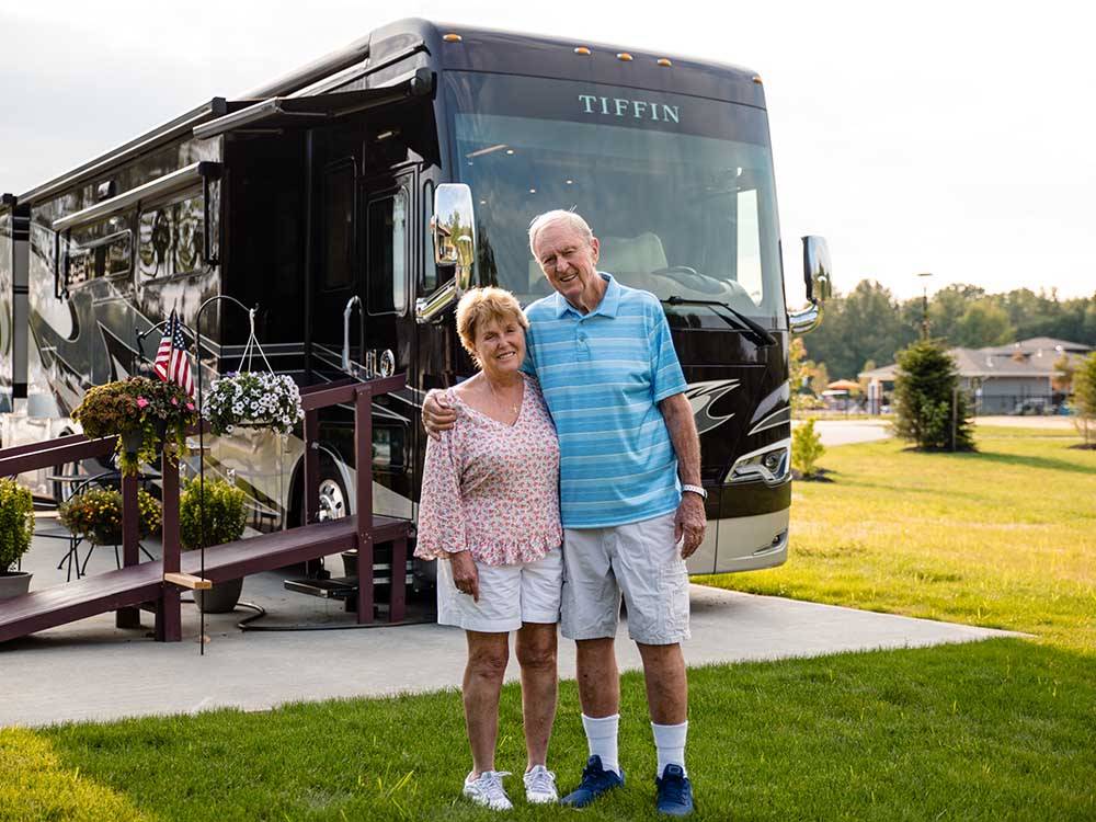 A couple standing in front of their RV at MOTORCOACH RESORT LAKE ERIE SHORES