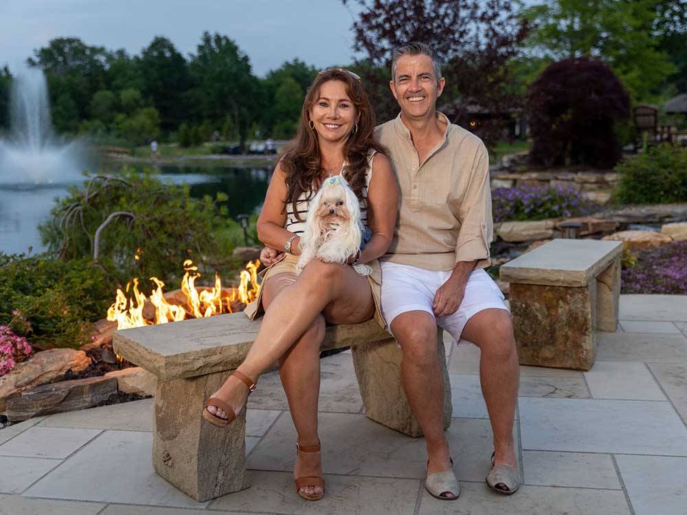 A couple and their dog sitting next to an open fire at MOTORCOACH RESORT LAKE ERIE SHORES