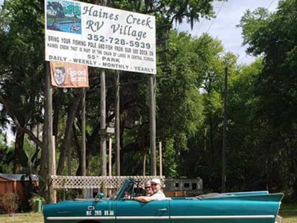 A couple in a car passing the front entrance sign at HAINES CREEK RV PARK