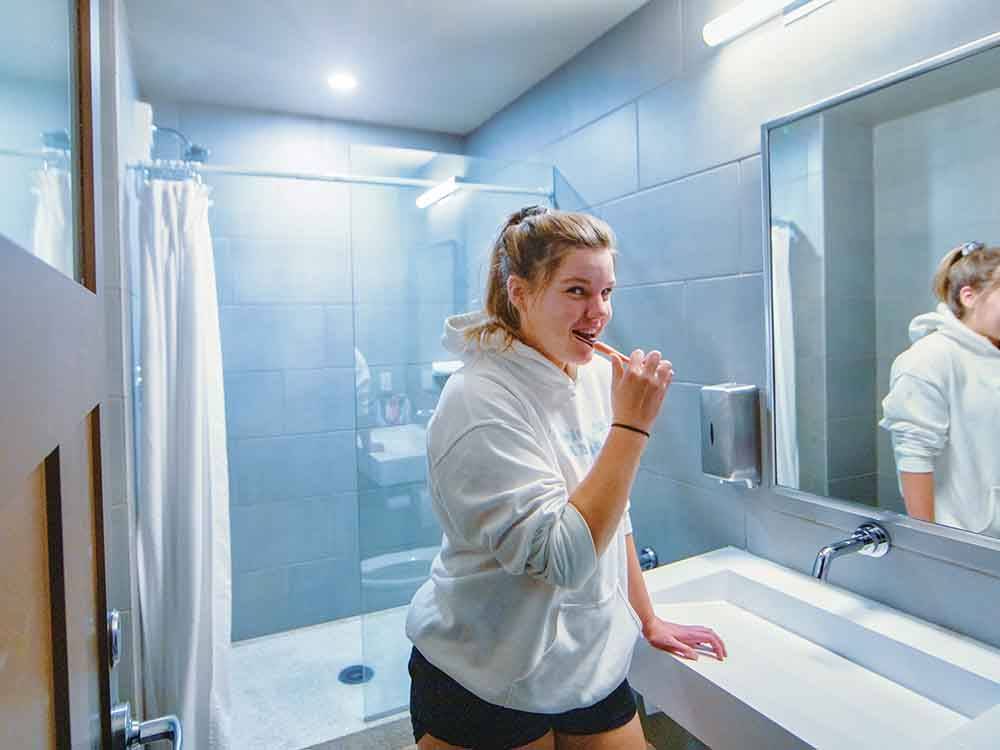 Woman in hoodie brushing teeth in tiled bathroom at CANYON VIEW RV RESORT