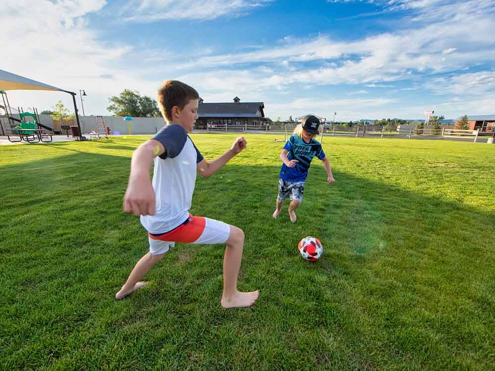 Two kids playing soccer on expansive grass field at CANYON VIEW RV RESORT