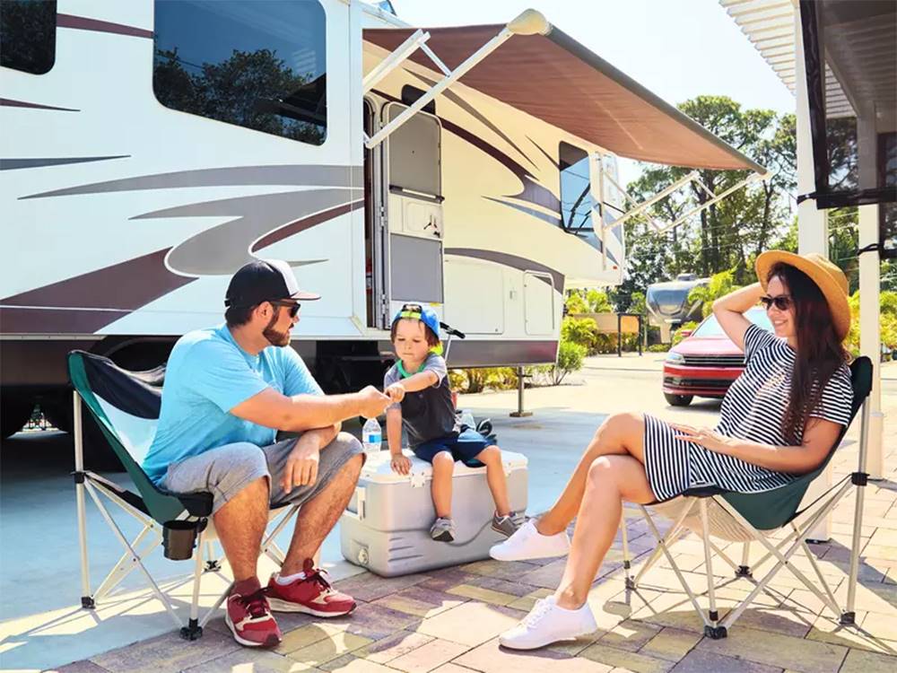 Family sitting outside their RV on a sunny day at an RV site