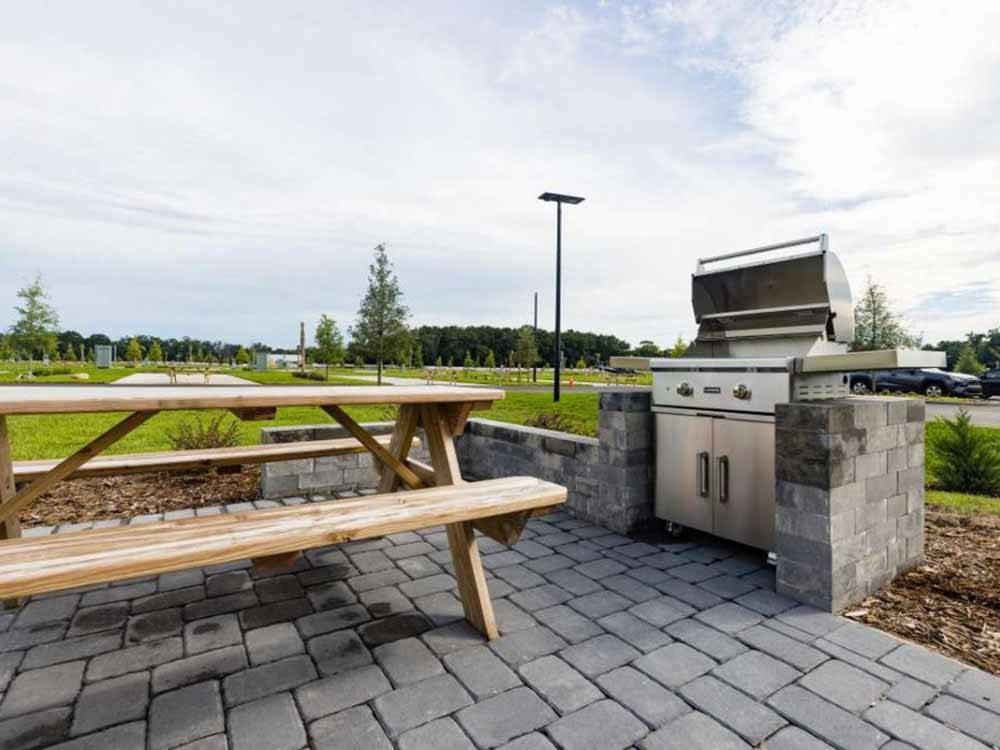 A picnic bench next to a barbecue pit at CHAMPIONS RUN LUXURY RV RESORT