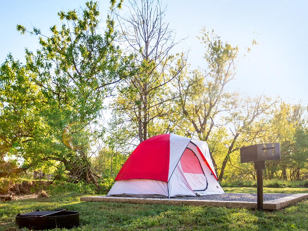 Red and white tent on a gravel site with a bbq pit at PIGEON FORGE LANDING RV RESORT