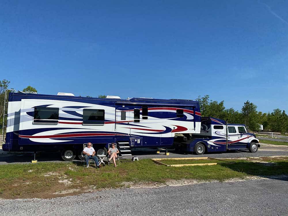 A couple sitting along side of a very large fifth wheel trailer at BIG RIG FRIENDLY RV RESORT