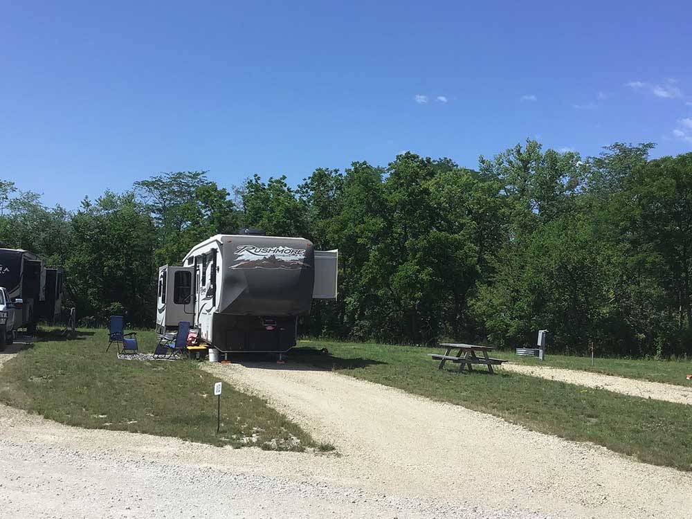 Rushmore fifth-wheel parked in site with patio chairs at CROWS NEST RV RESORT