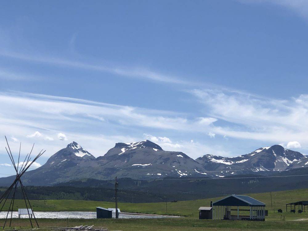 A tipi being built with mountains in the distance at Buffalo Calf Campground