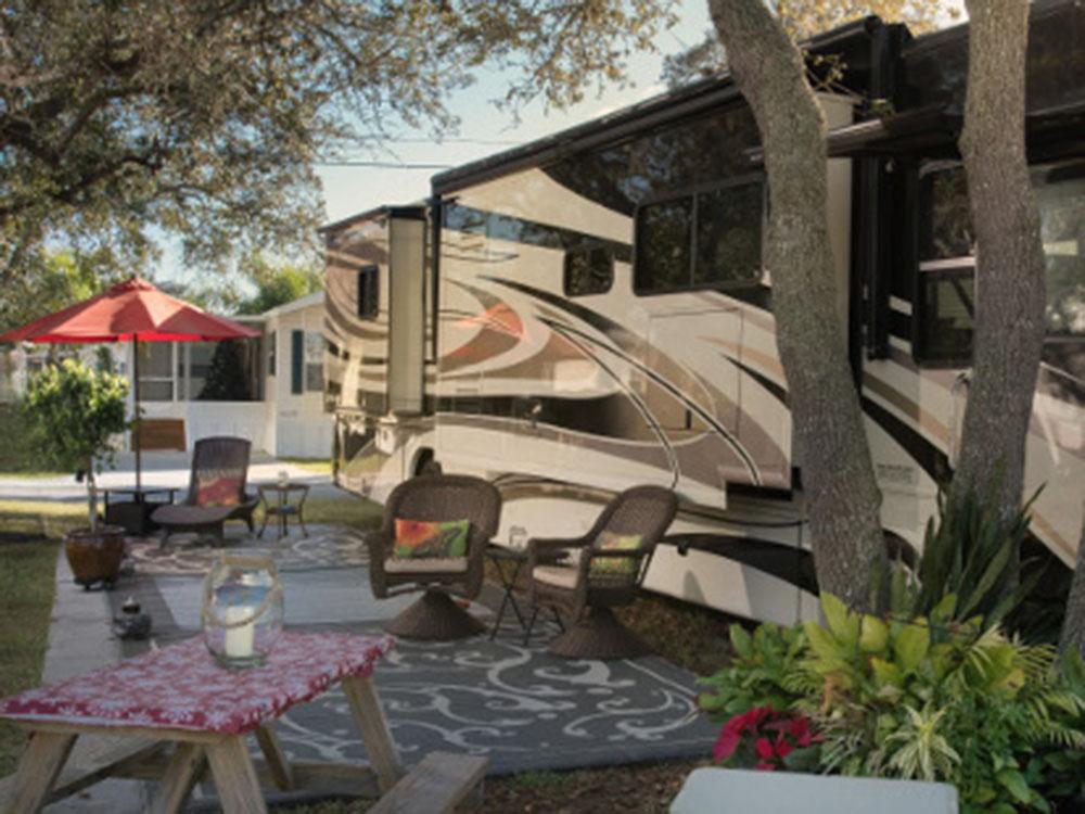 Exterior of RV with surrounding picnic table and chairs under the tree at OCEAN GROVE RV RESORT