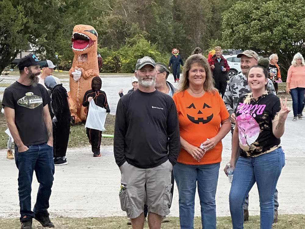 A group of people standing around with a T-Rex sneaking up behind them at BUTTON'S FAMILY CAMPGROUND