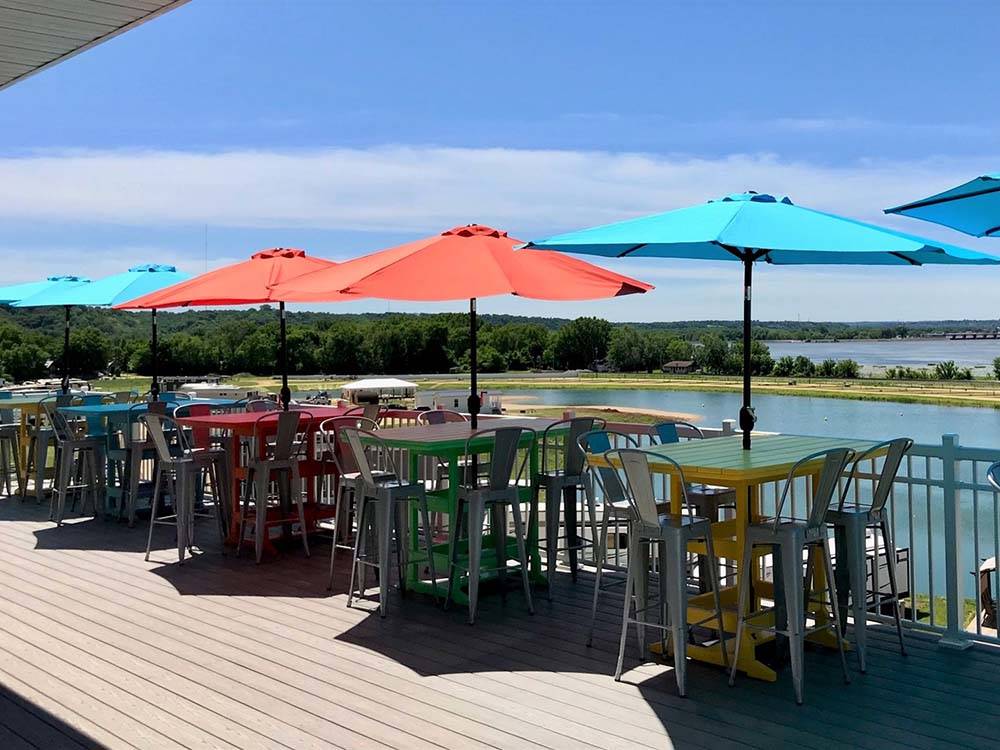 Tables and stools with umbrellas overlooking the lake at COCONUT COVE RV RESORT BY RJOURNEY