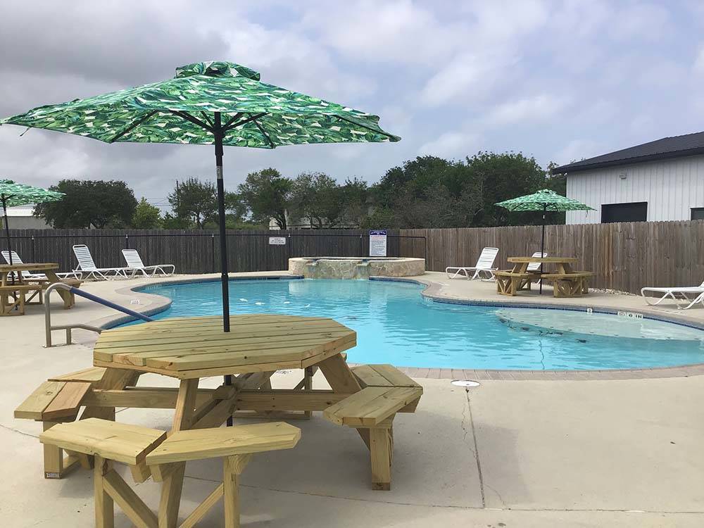 A table with an umbrella next to the swimming pool at PORT O'CONNOR RV PARK
