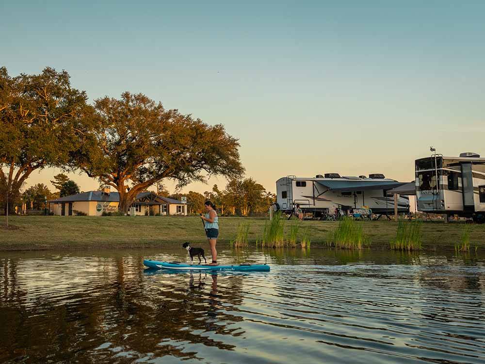 A woman and her dog paddling on a board at GULF SHORES RV RESORT
