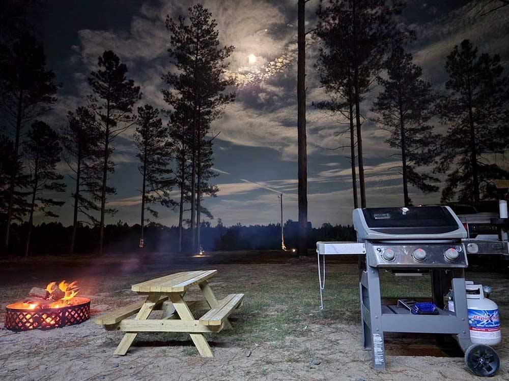 A barbecue pit and bench next to a fire pit lit at DREAM RV PARKS