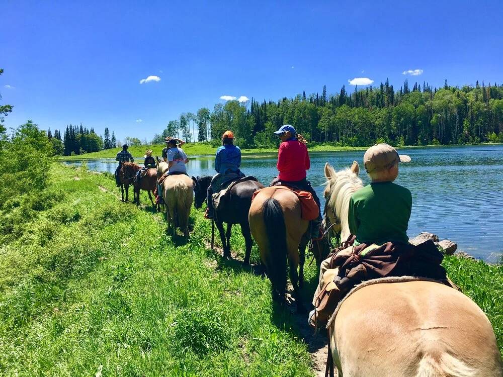 Family horseback riding alongside a river