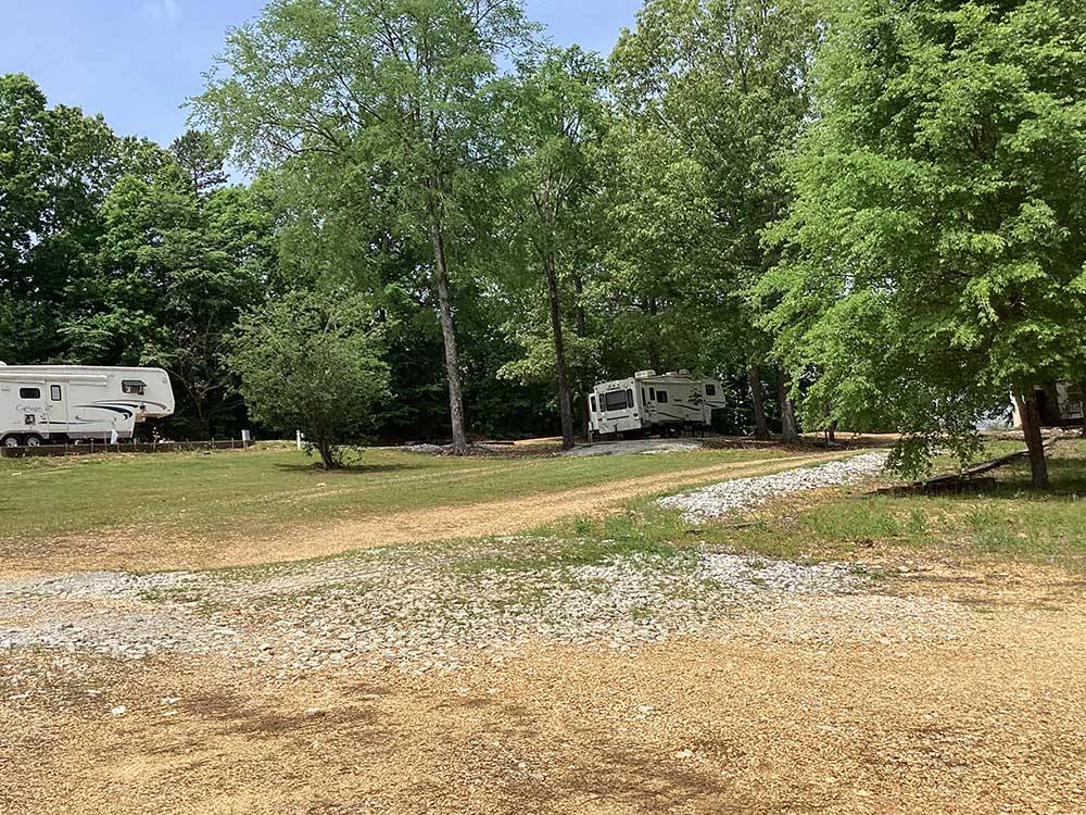 Travel trailers parked in gravel sites next to tall trees at CORINTH RV PARK
