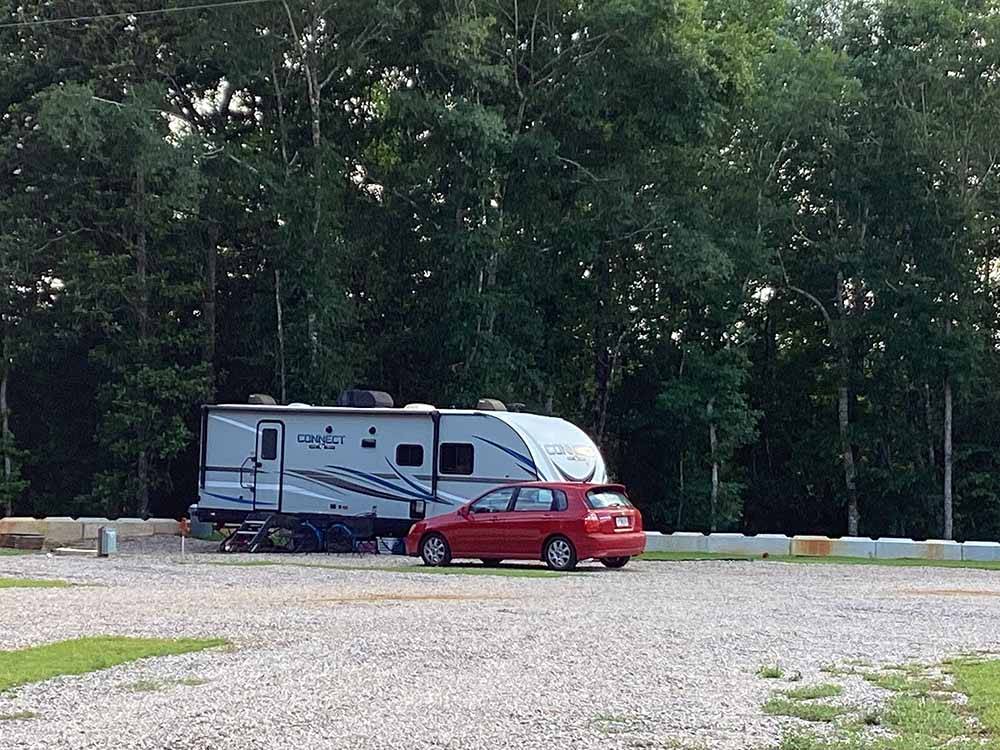 A red car and trailer parked in a site at KELLY CREEK RV PARK
