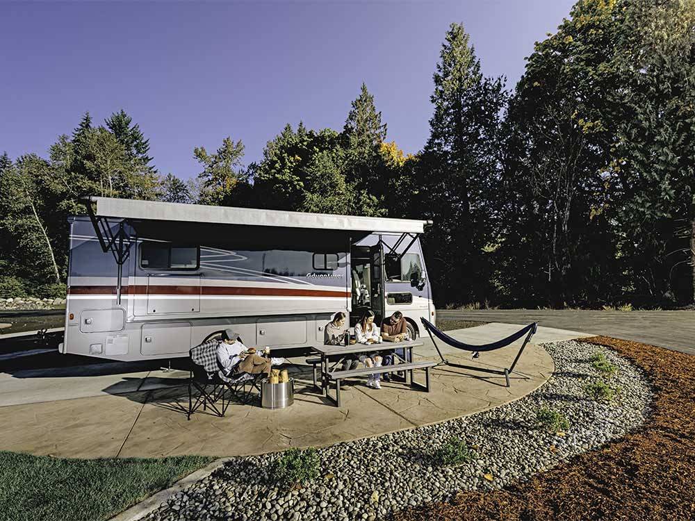 A family sitting in front of their RV in a paved site at ANGEL OF THE WINDS RV RESORT