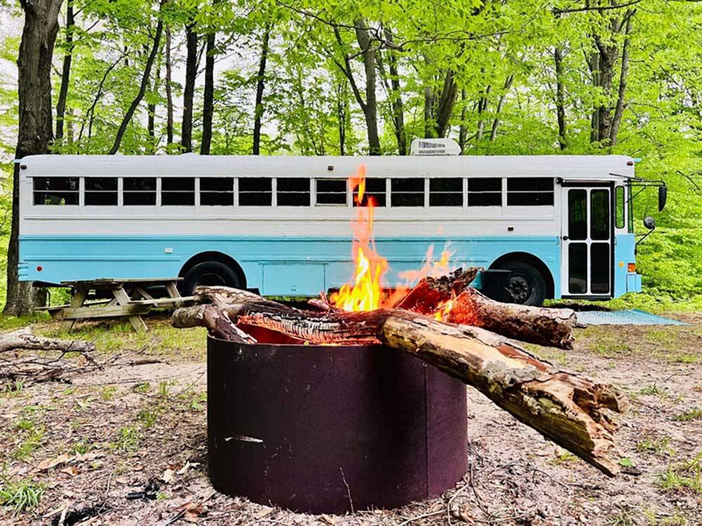 A burning fire pit with a bus in the background at DANCING FIRE GLAMPING AND RV RESORT
