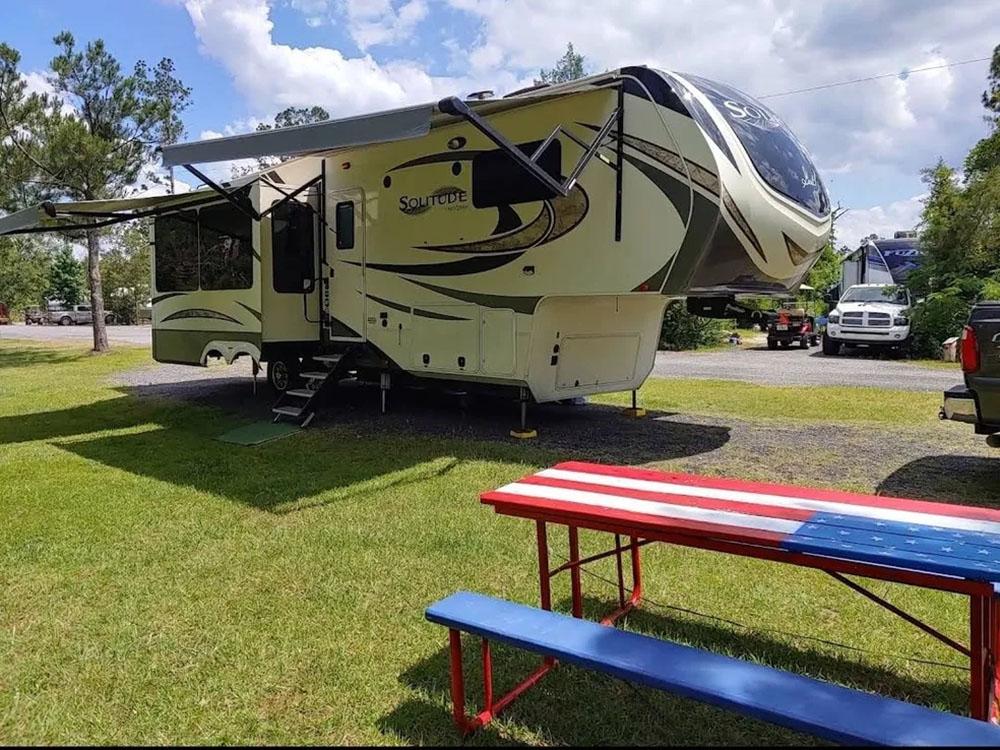 Red, white and blue picnic table and fifth wheel in camp site at HITCHINPOST RV PARK AND CAMPGROUND