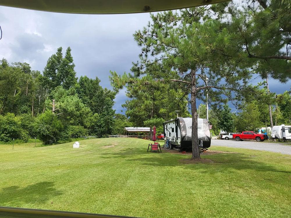 Tree lined and grassy camp site with RV at HITCHINPOST RV PARK AND CAMPGROUND