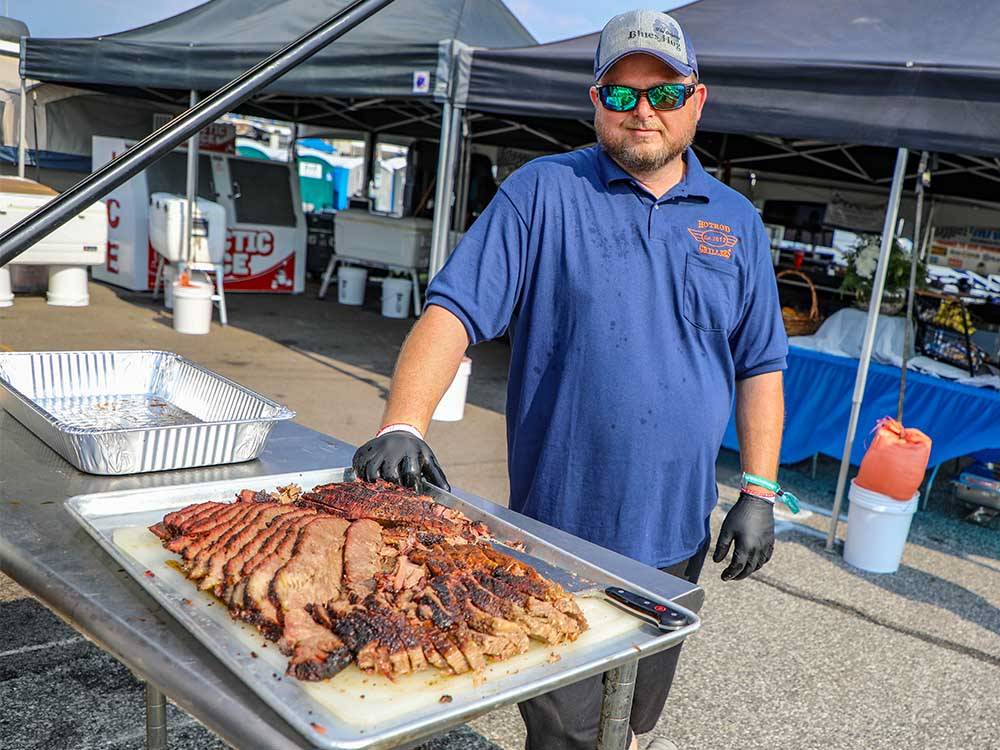 A man standing next to some bbq food at WORLD WIDE TECHNOLOGY RECEWAY CAMPGROUND