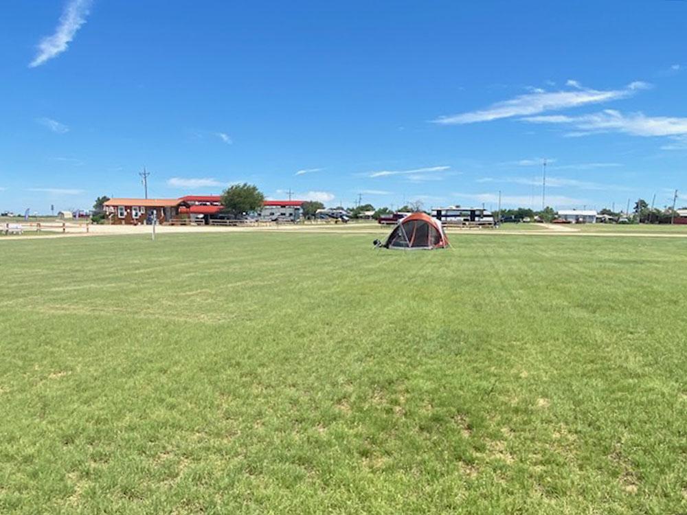 A tent pitched in an open grassy field at SILVER WIND RV PARK AND CABINS