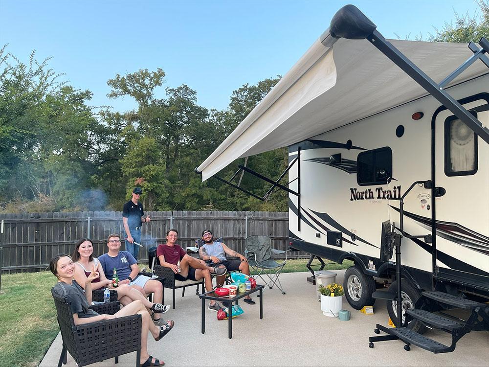 A family sitting next to their trailer at TIMBER RIDGE RV PARK