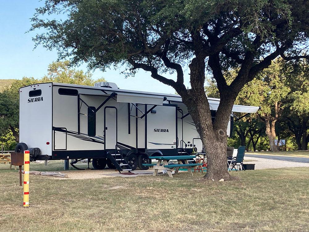 Large travel trailer near a shade tree at LOST MAPLES RV AND CAMPING