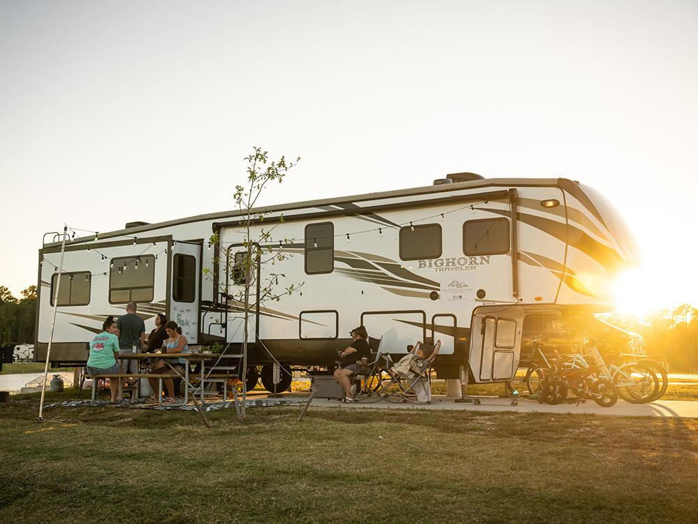 Family sits at a picnic table in front of a 5th wheel at SANDUSKY RV RESORT