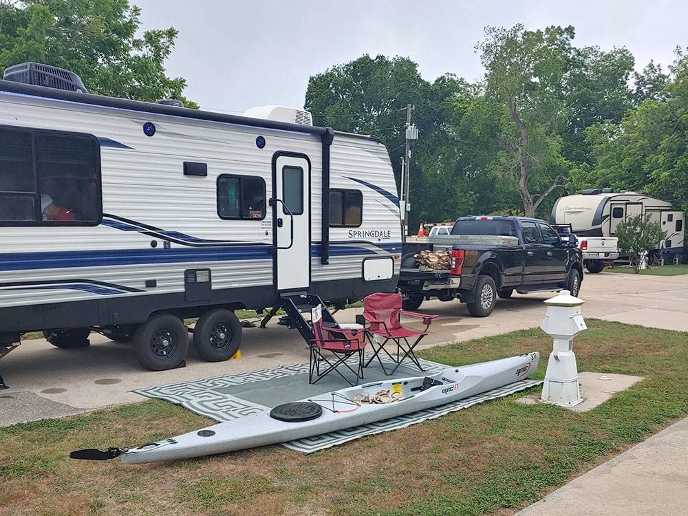 An RV parked at site with seating and kayak
