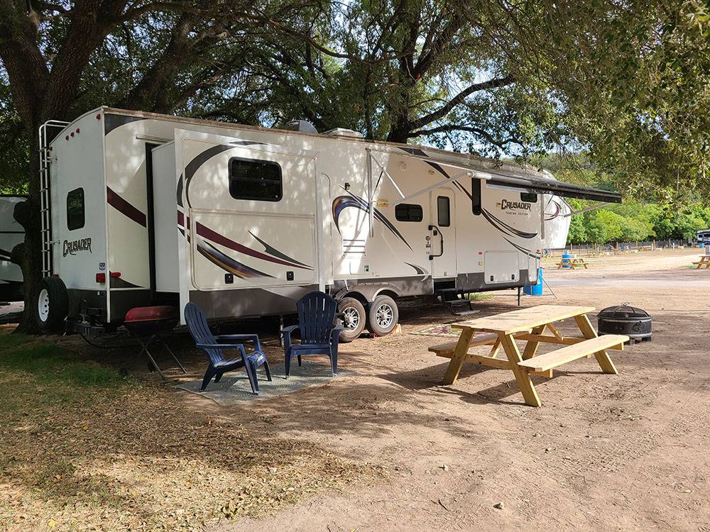 An RV, picnic table and chairs in a shaded site